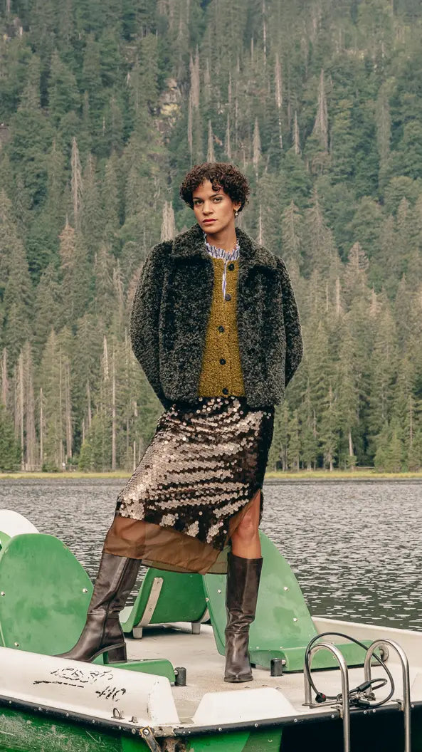 Frau auf Tretboot trägt Plüschjacke über Steppweste und Streifenhemd, Pailletten-Rock und hohe Lederstiefel – Herbst-Outfit 2026 von FREY Mode