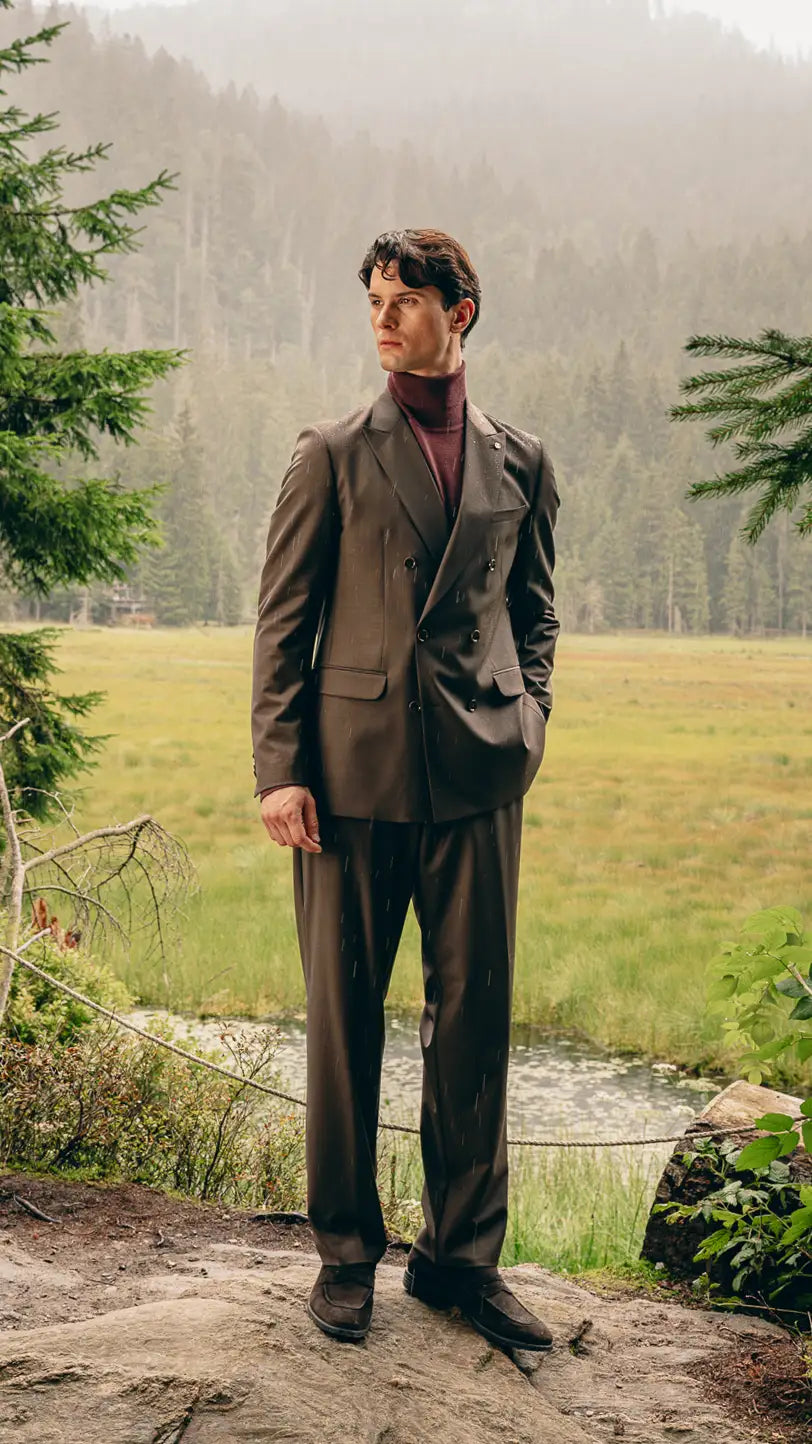 Mann steht im Grünen in braunem Anzug mit Bordeaux-Pullover, moderne Interpretation eines Herbst-Anzugs – Herbst/Winter-Outfit 2026 von FREY Mode