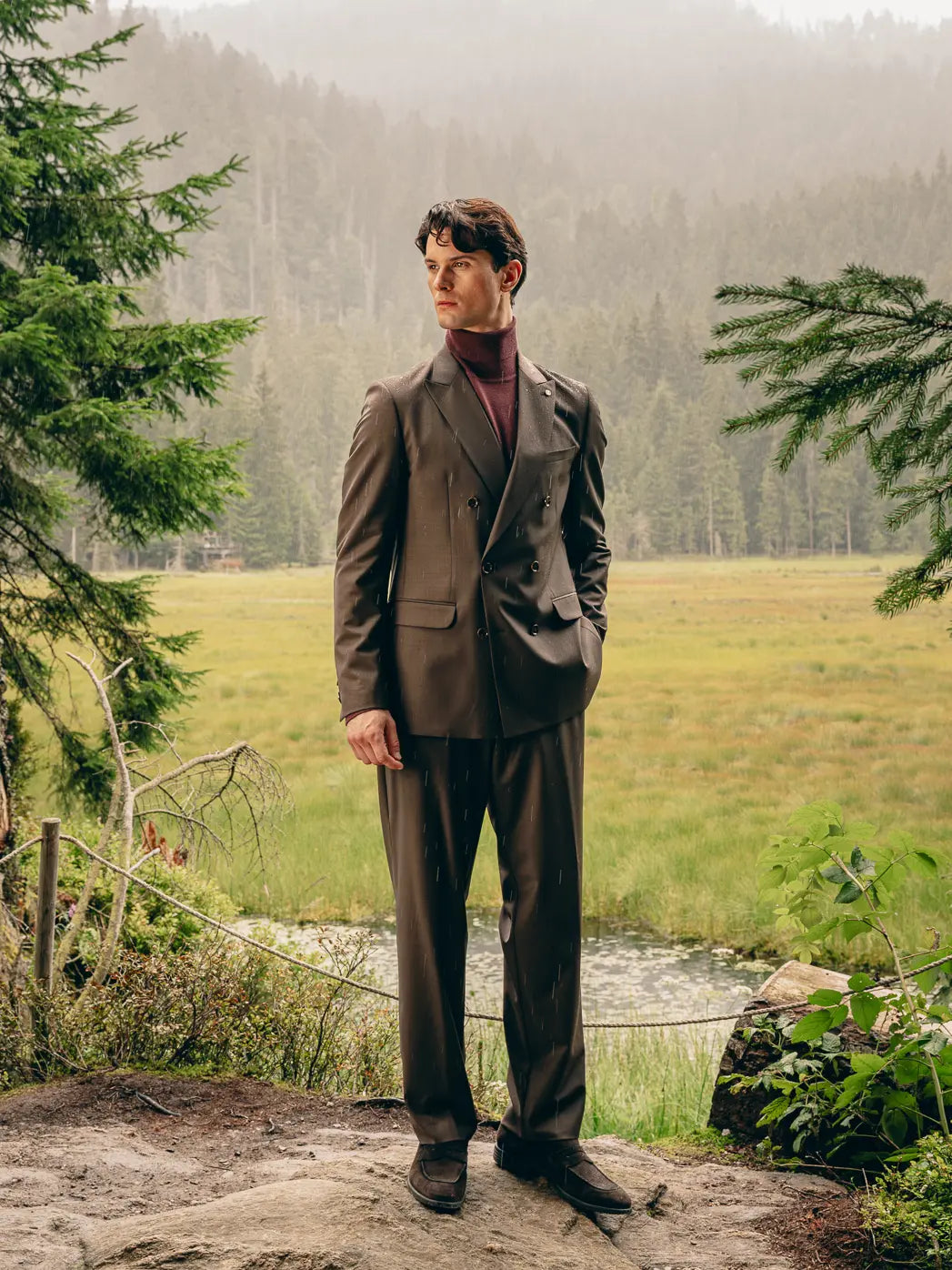 Mann steht im Grünen in braunem Anzug mit Bordeaux-Pullover, moderne Interpretation eines Herbst-Anzugs – Herbst/Winter-Outfit 2026 von FREY Mode