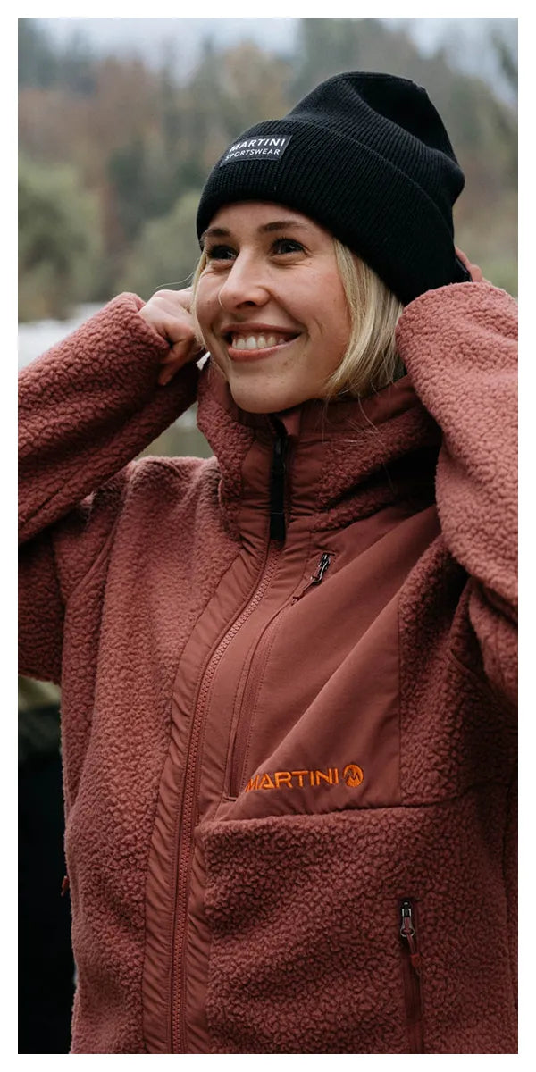 Frau mit schwarzer Mütze und rostroter Fleecejacke.