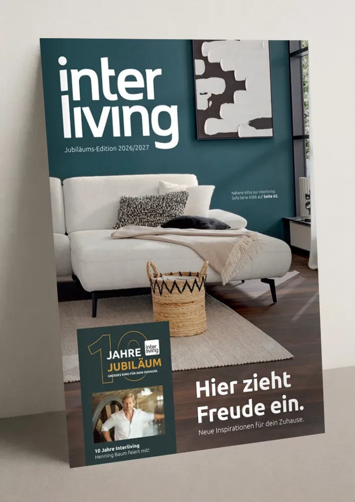 Titelseite des Interliving Wohnbuchs, Jubiläums-Edition 2026/2027: helles Sofa vor petrolfarbener Wand, Slogan „Hier zieht Freude ein."