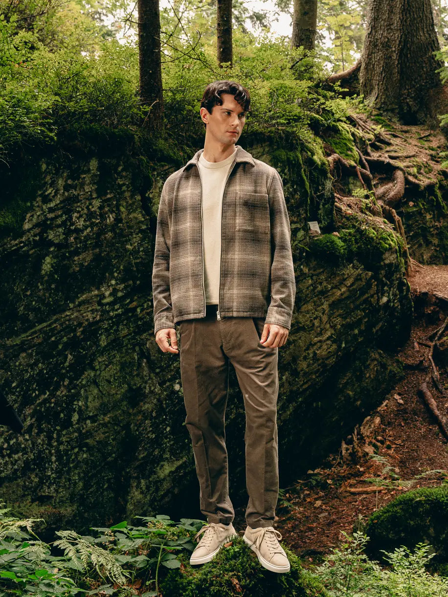 Mann steht im Wald in kariertem Urban-Heritage-Look mit Harrington-Jacke, Pullover und Cordhose – Herbst/Winter-Outfit 2026 von FREY Mode