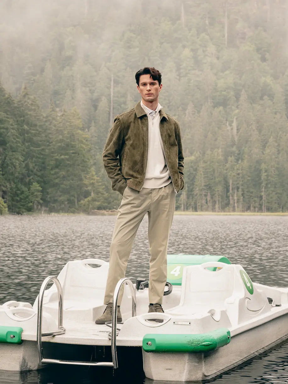 Mann auf Tretboot trägt grüne Veloursleder-Jacke über cremefarbenem Pullover und Streifenhemd, beige Hose und Stiefeletten – Herbst-Outfit 2026 von FREY Mode