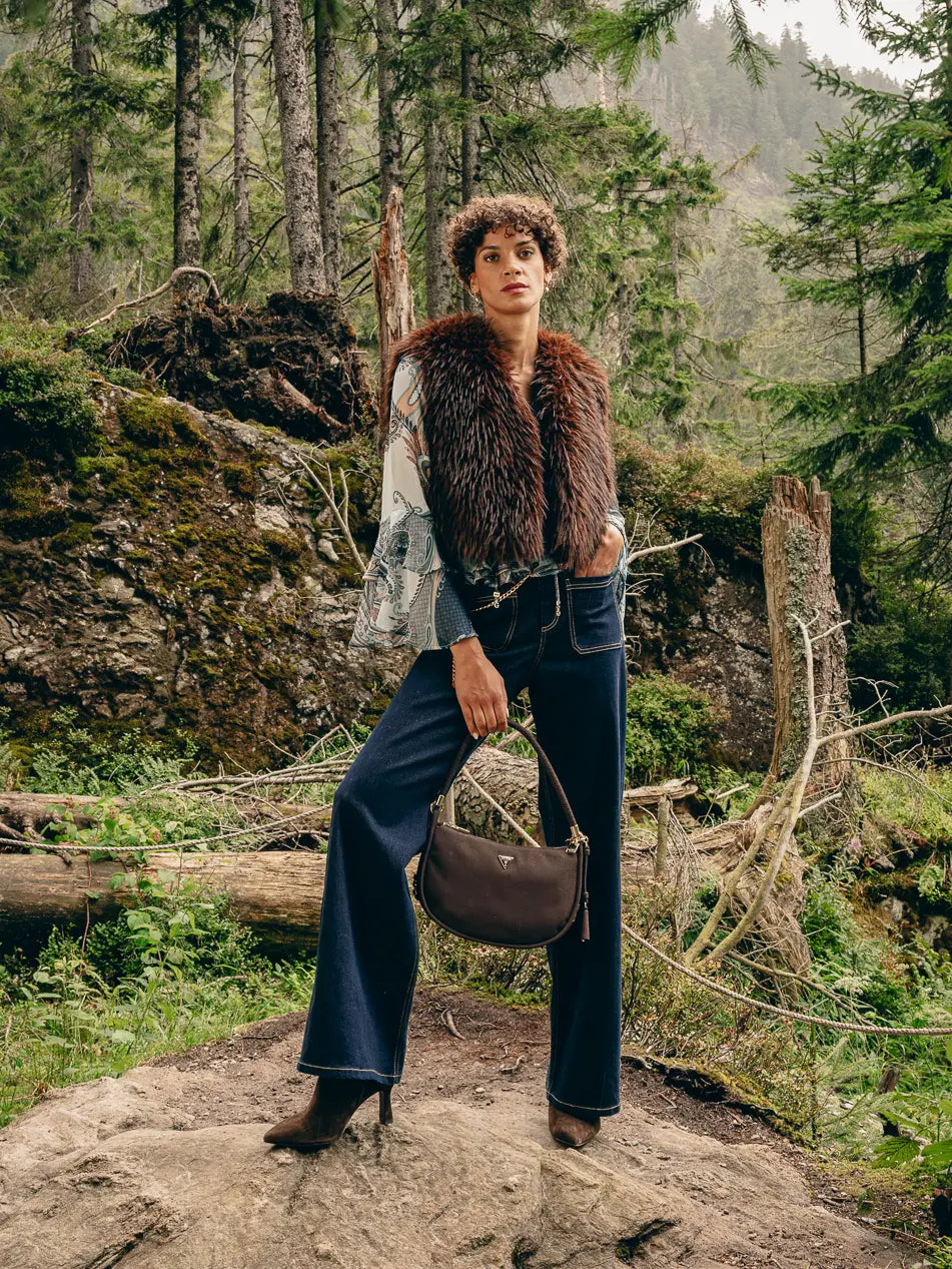 Frau im Wald trägt braune Kunstfellweste, Volant-Bluse und dunkelblaue Wide-Leg-Jeans – Herbst-Outfit 2026 von FREY Mode