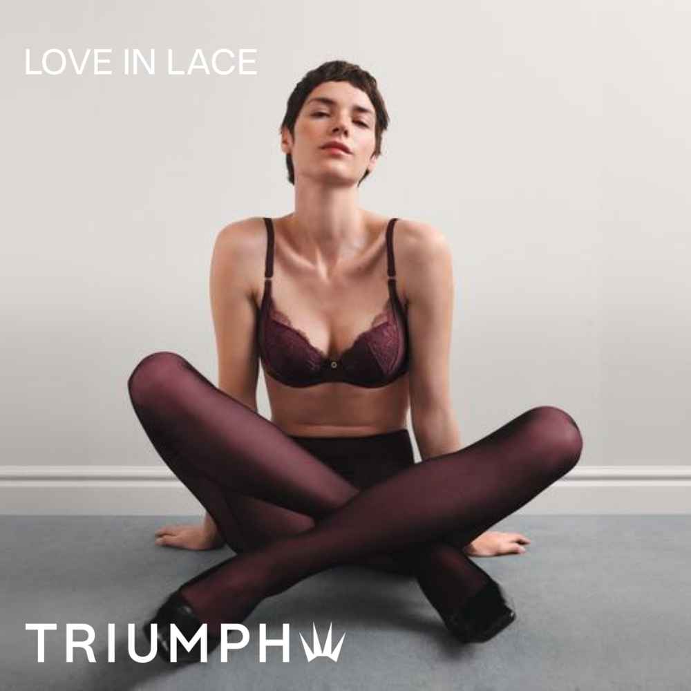 Model im bordeauxfarbenen Spitzen-BH und dunkler Strumpfhose, sitzend mit überkreuzten Beinen – Kampagnenmotiv „Love in Lace“ von Triumph.