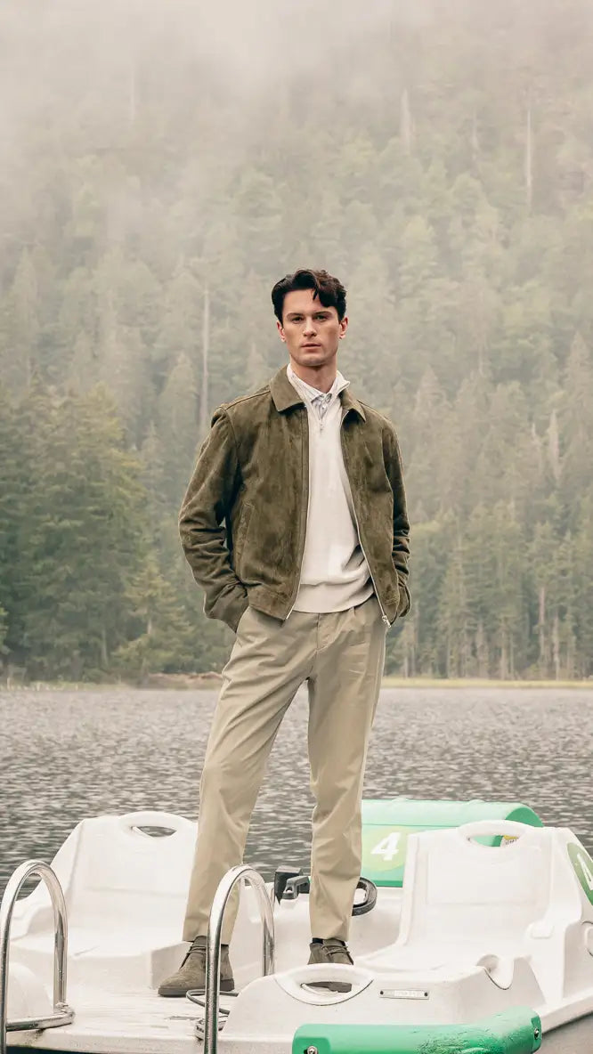 Mann auf Tretboot trägt grüne Veloursleder-Jacke über cremefarbenem Pullover und Streifenhemd, beige Hose und Stiefeletten – Herbst-Outfit 2026 von FREY Mode