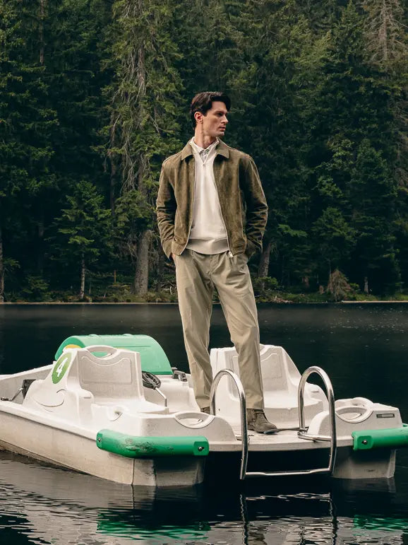 Mann steht auf Tretboot im Wald in Waldgrün-Look aus Veloursleder-Jacke, Pullover und Hose mit grünen Stiefeletten von Lloyd – Herbst/Winter-Outfit 2026 von FREY Mode