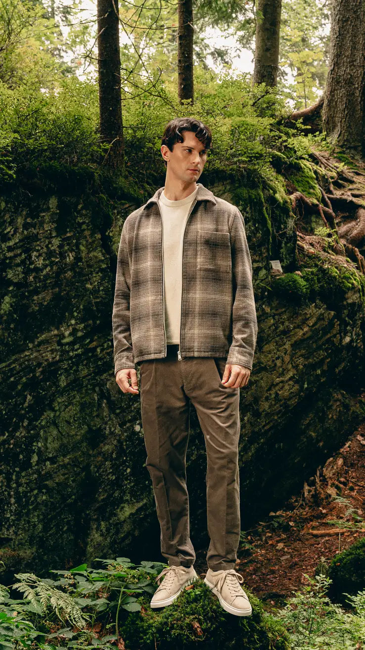 Mann steht im Wald in kariertem Urban-Heritage-Look mit Harrington-Jacke, Pullover und Cordhose – Herbst/Winter-Outfit 2026 von FREY Mode